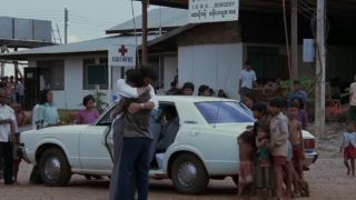 Two men hugging in front of a white car in The Killing Fields