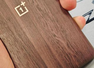 A hand holding a smartphone with a OnePlus logo, with what appears to be wooden back
