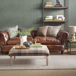 a leather sofa in the centre of a living room, with green wallpaper, a beige carpet and a stone rug runner