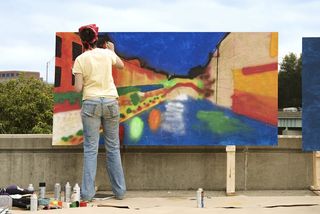 An artist paints an outdoor mural.