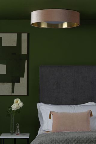 green bedroom with artwork, grey headboard, velvet and gold ceiling light