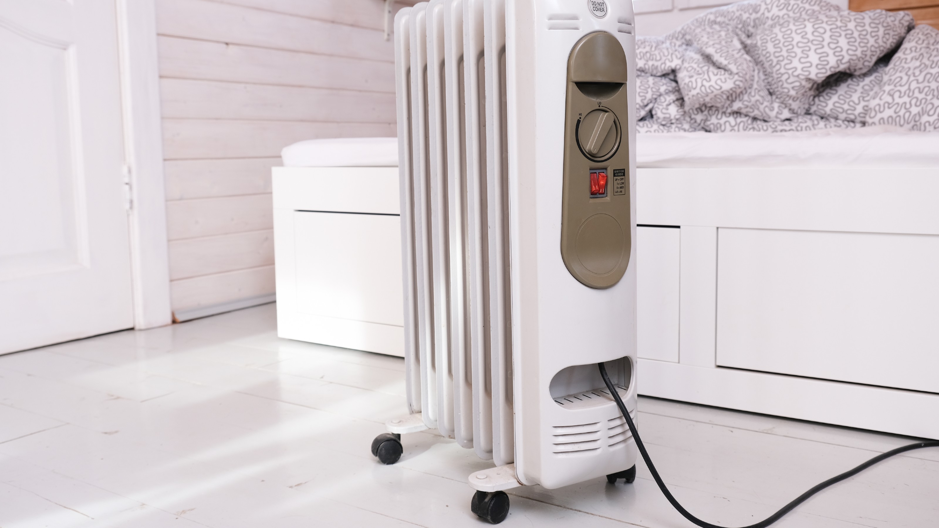 oil-filled radiator in a wood clad room, in front of a day bed with a blanket