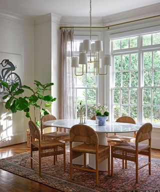 A brightly lit dining room with woven chairs and a vintage-inspired rug