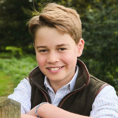 Prince George wearing a vest smiling and leaning on a fence