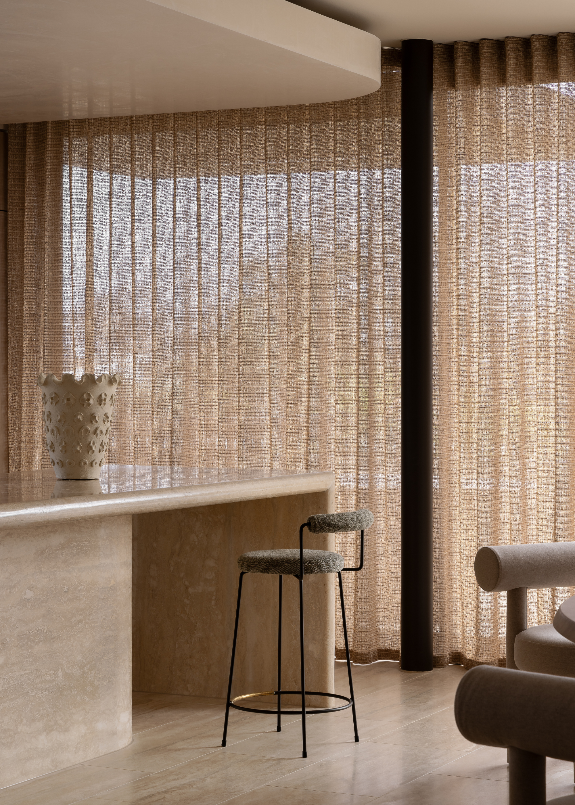 A minimalist kitchen with sheer window treatments, a stone kitchen island, a metal bar stool, a textured vase, and a sofa seater