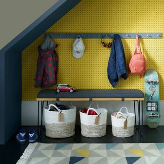 Yellow dry-wall with a sitting bench and a clothing rack, personalized name baskets and toys