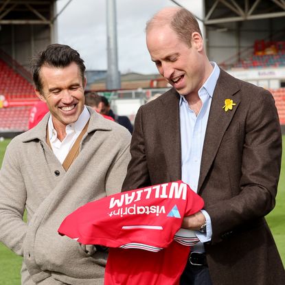 Chairman of Wrexham AFC Rob McElhenney and Prince William, Prince of Wales with his personalised Wrexham AFC shirt on the pitch at the Racecourse Ground after his visit to The Turf Pub, near Wrexham AFC as he marks St. David's Day on March 01, 2024 in Wrexham, Wales.