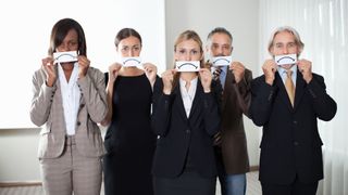 A group of unhappy employees holding drawings of unhappy expressions against their faces
