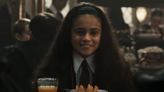 Arabella Stanton as Hermione Granger sitting in the Great Hall in the Harry Potter TV series.