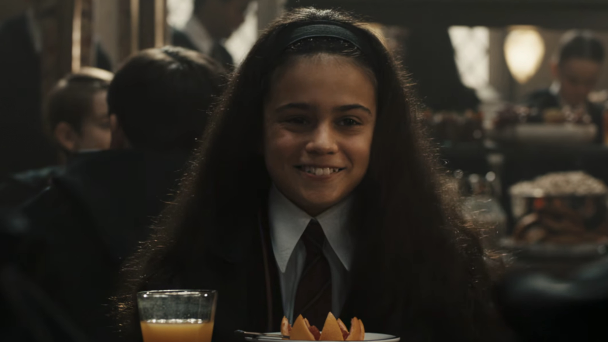Arabella Stanton as Hermione Granger sitting in the Great Hall in the Harry Potter TV series.