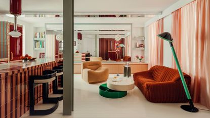 colorful kitchen with striped tiled countertop, reflective surfaces, structural column, pink curtains, a red velvet sofa, green and white coffee table, beige armchair, and green floor lamp