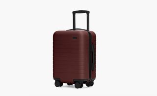 The Kids Carry-On luggage, by Away. A burgundy hard shell case on wheels with a black handle.