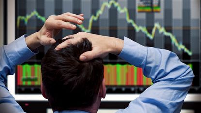 An investor puts his hands on his heads as he watches a stock market drop.