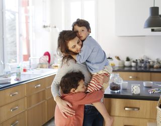 A woman hugging two boys in a kitchen