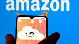 A hand holds a phone bearing the AWS logo, while the Amazon logo shows in the background