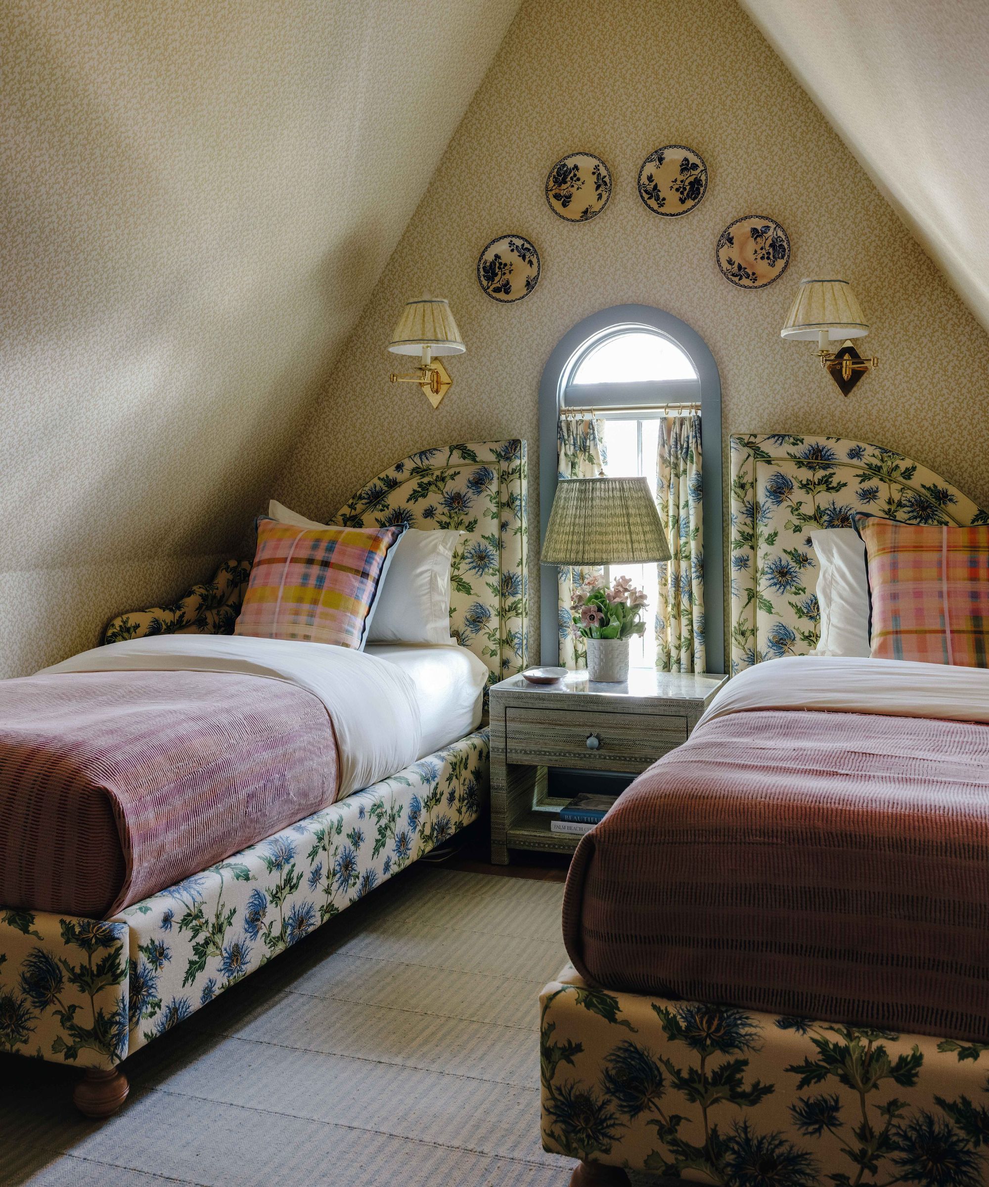 a subtle ditsy wallpapered loft bedroom with angled ceiling, two twin floral beds with matching curtain checked bedding and wall plates