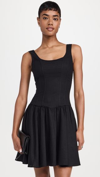 A model wears a black sleeveless round neck mini dress with a pleated skirt.