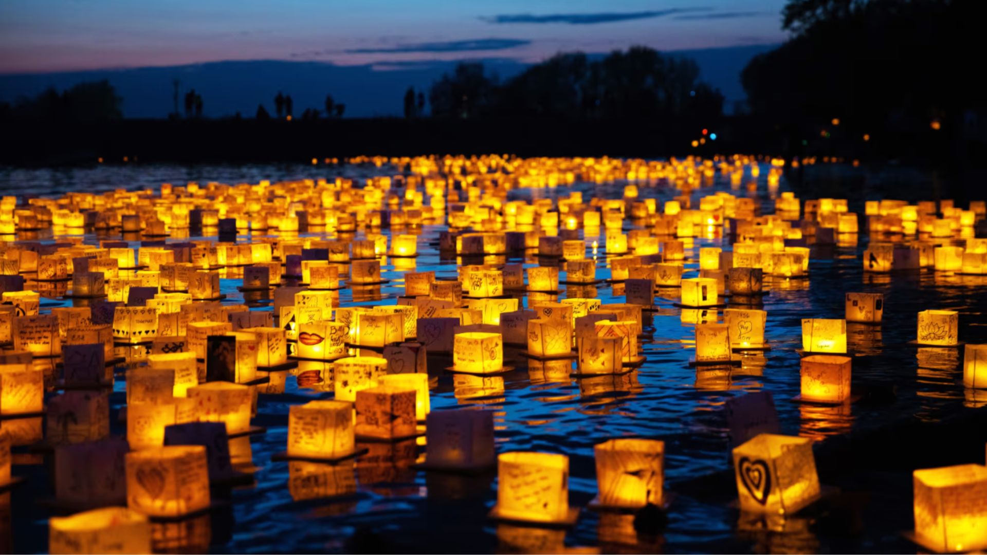 an image of hundreds of glowing lanterns floating on a large lake at dusk