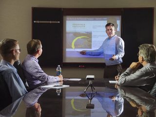 A man delivers a slideshow presentation to colleagues in a meeting. room.