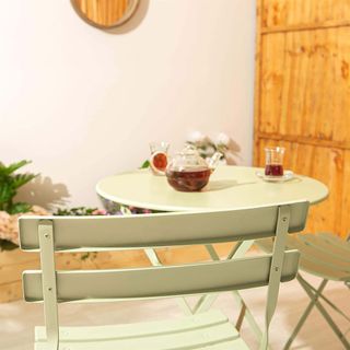 Sage green bistro table and chairs with coffee on in garden.