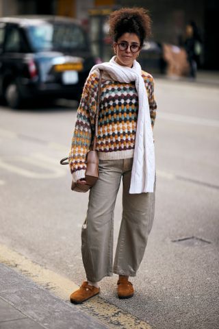 a guest attends london fashion week fall/winter 2024 wearing a multicolor striped sweater and grey jeans white scarf