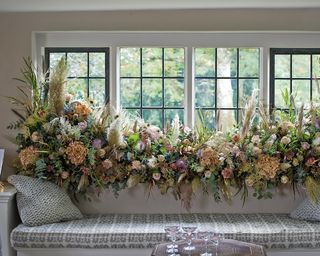 Christmas window decor ideas with a large floral display in pastel colors running the length of a window sill above a bench