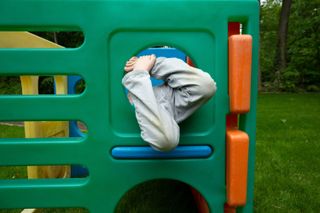 A child on a climbing frame with grass stains on their jeans