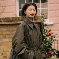 A woman walks along a London street wearing an olive raincoat