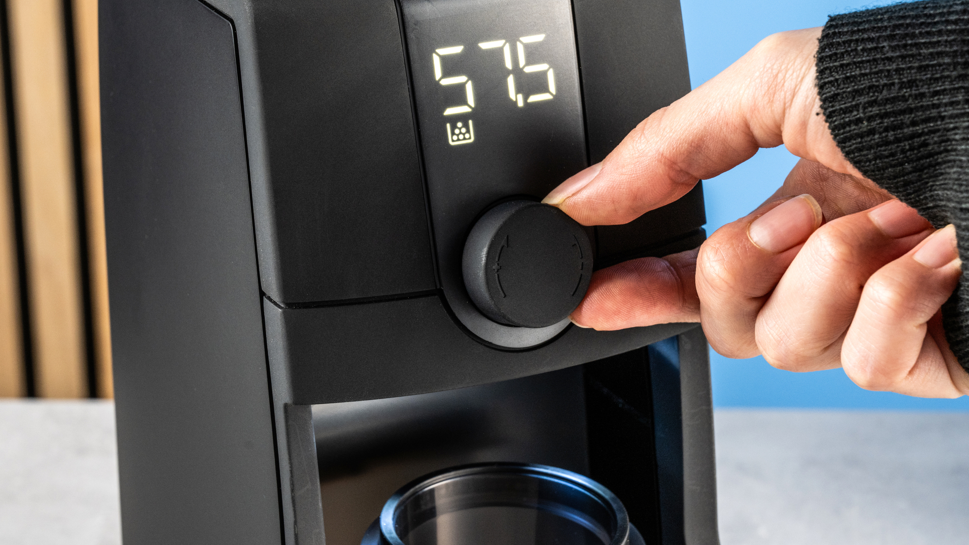 the baratza encore esp pro coffee grinder photographed against a blue tom's guide background with a bag of coffee to the side and showing the grinder in action