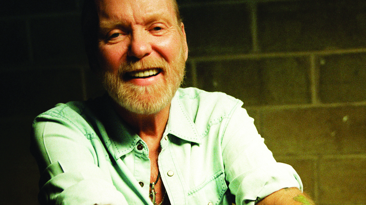 Gregg Allman in a pale green shirt looking at the camera and smiling.