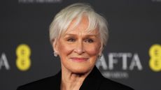 Image of Glenn Close smiling with grey hair pixie cut, rosy pink lipstick and square diamond earrings