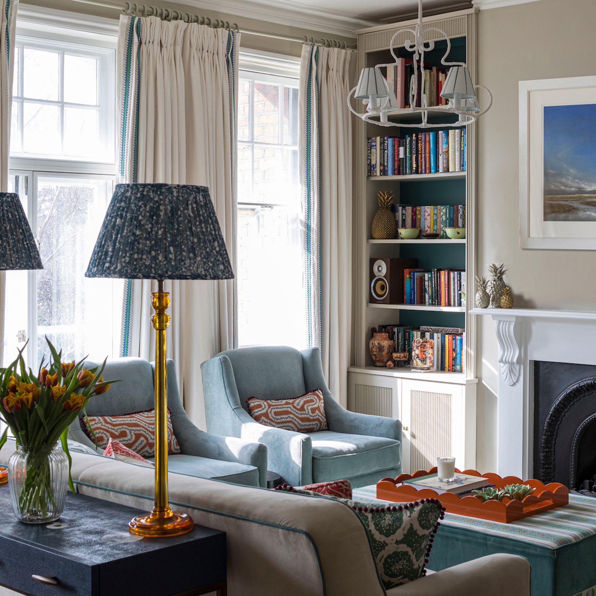 Cream living room with blue armchairs, striped ottoman and built in bookcase