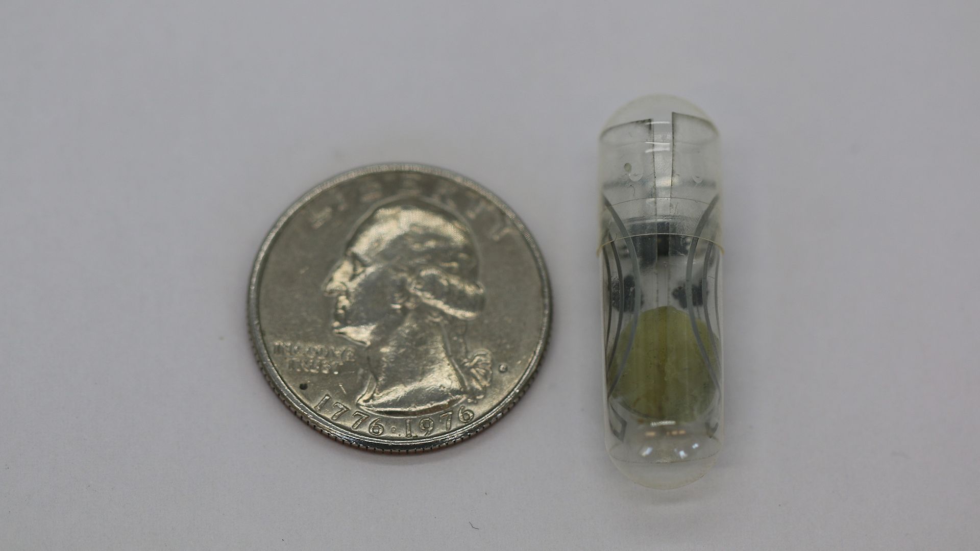 A quarter next to a small pill against a gray surface.