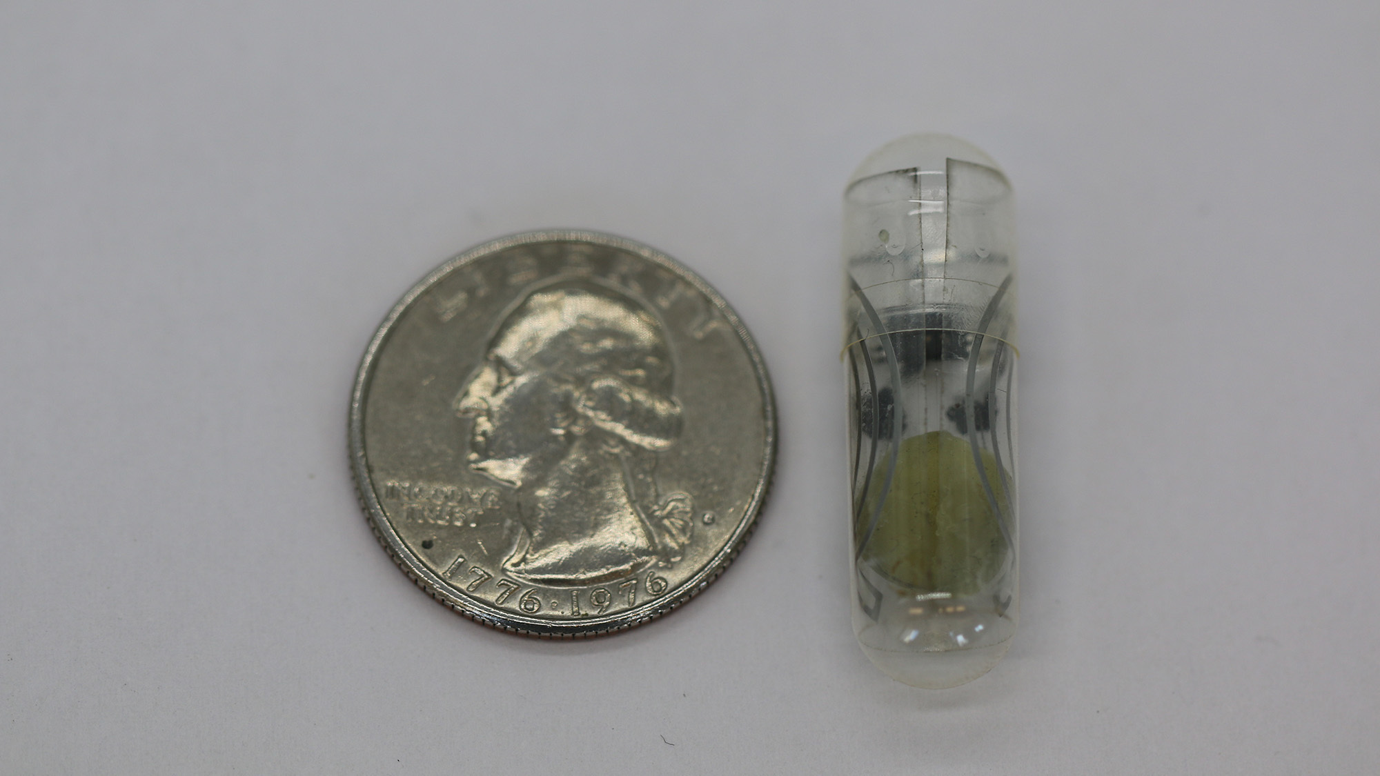 A quarter next to a small pill against a gray surface.
