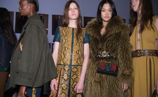 2 female models in snake skin & fur coats pose for the camera in busy studio