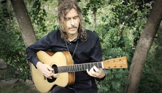 Mikael Åkerfeldt plays his new signature Martin acoustic guitar, with lush greenery behind him