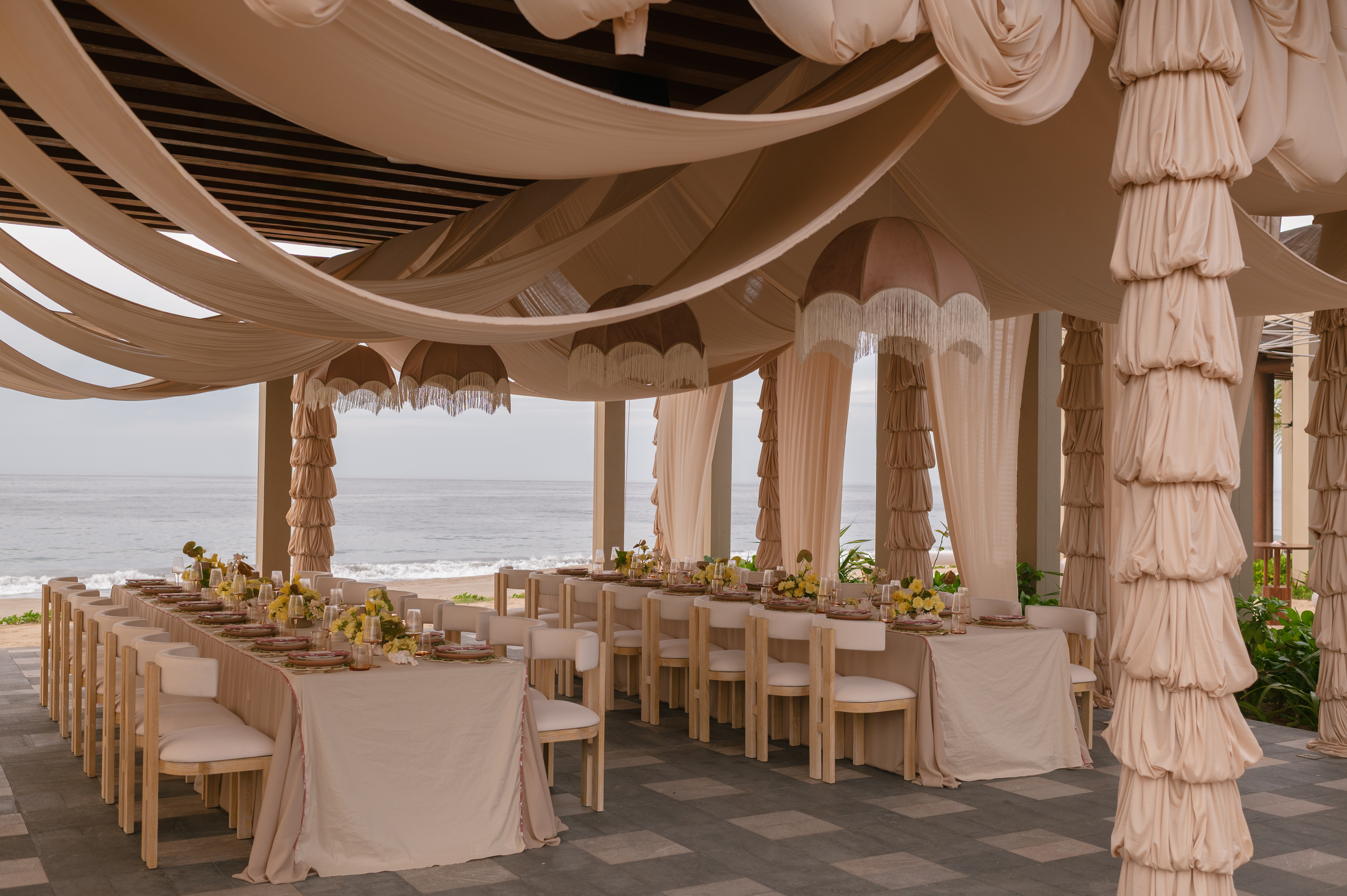 A sea-view restaurant draped in nude-tone fabric and decorated with natural flowers.