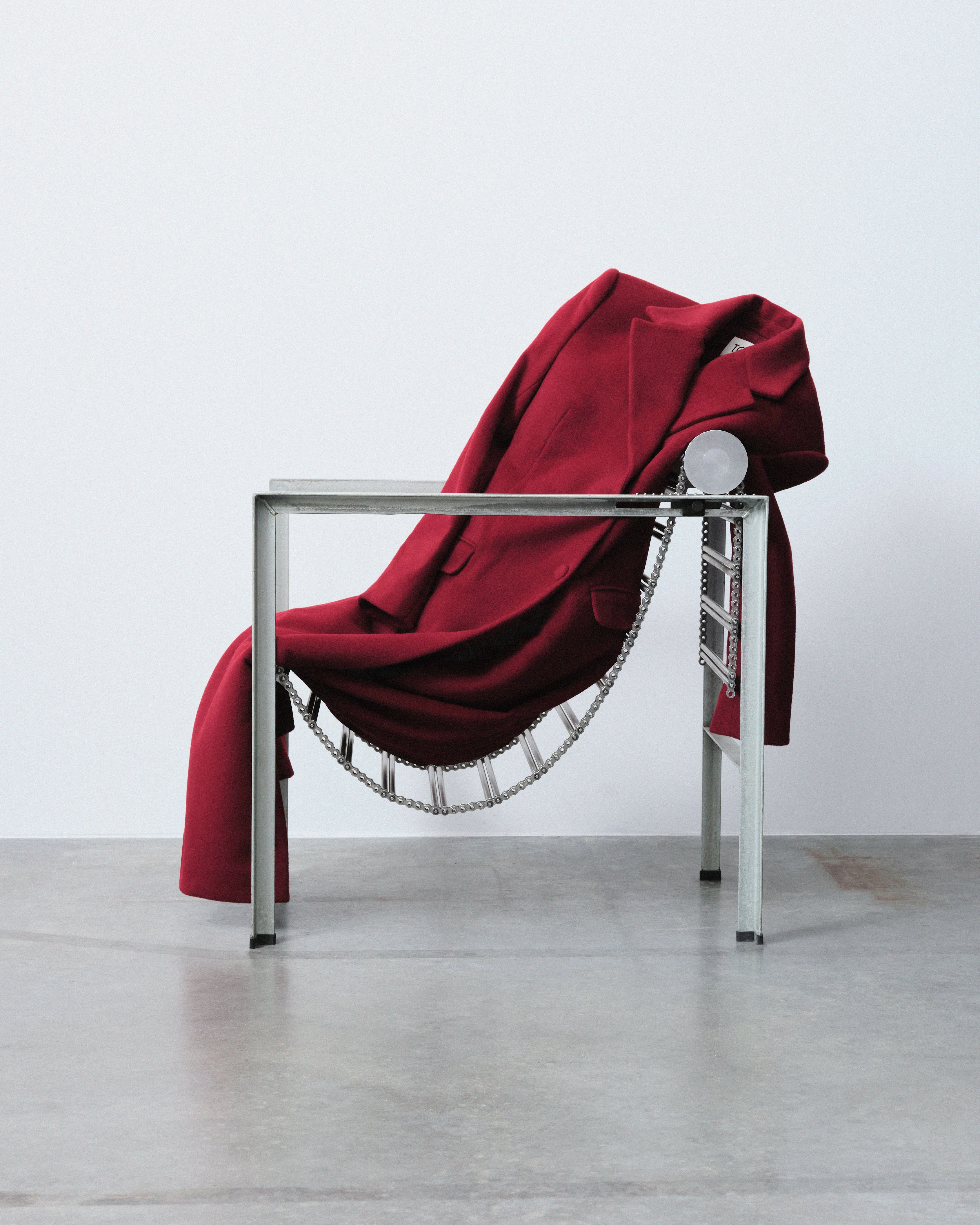 A chrome chair with a chain-like structure is topped by a red coat in an industrial site.