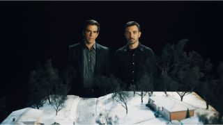 Exec producers Eli Roth (left) and Branden Morgen (right) stand behind a snow-covered model set of Jefferson, New Jersey in a promotional image for "Let the Devil In".