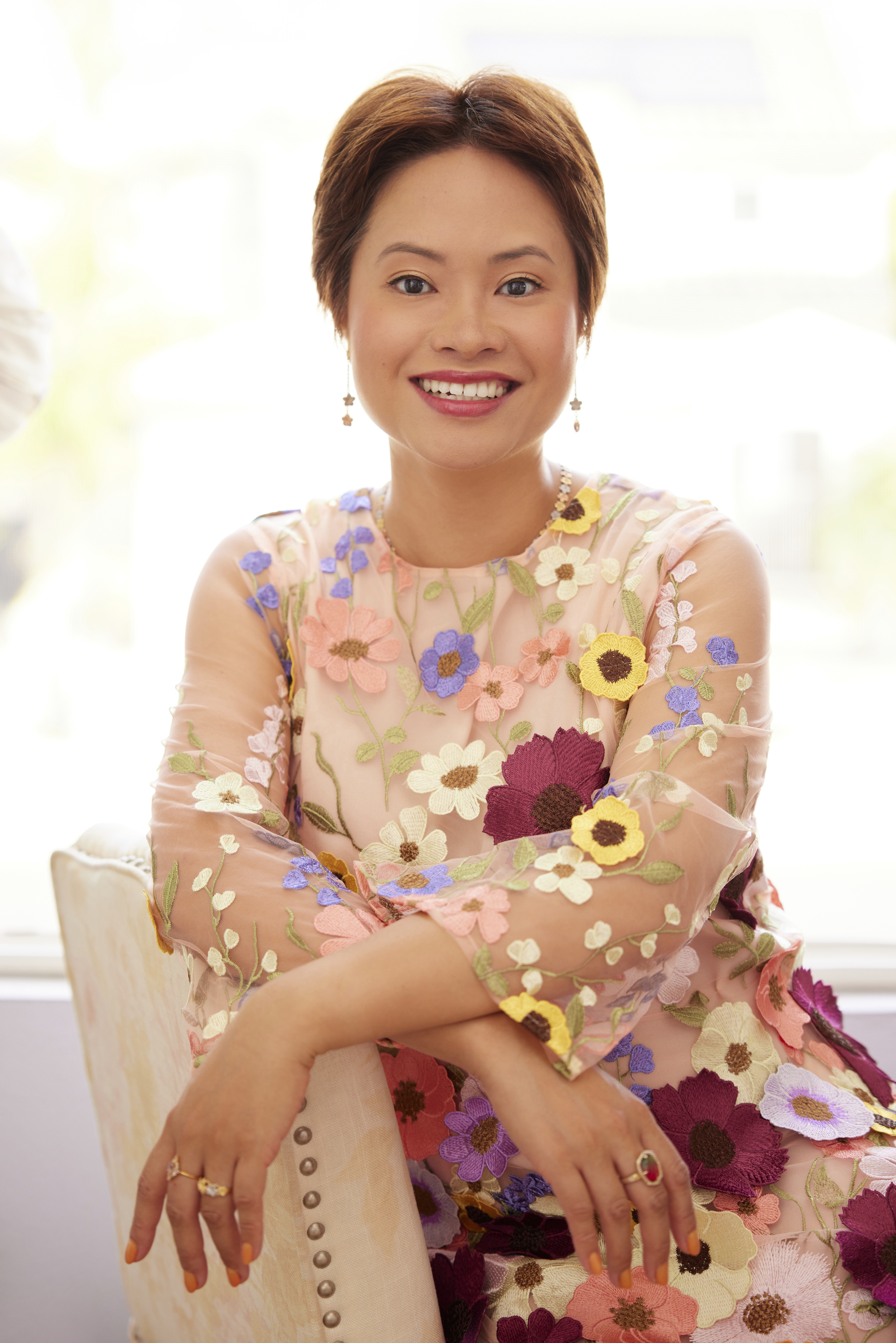 A woman in a floral dress and cropped brown hair smiling at the camera 