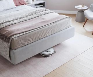 An ECOVACS robot vacuum cleaning beneath a bed.