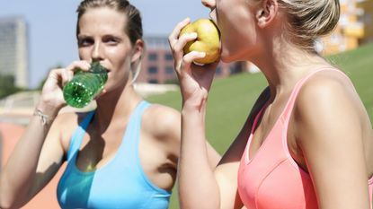 Fit women with pre-workout snacks (drinking water and eating a pear)