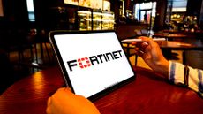 Fortinet logo and branding pictured on a tablet screen held by man in coffee shop.