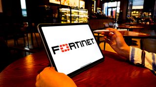 Fortinet logo and branding pictured on a tablet screen held by man in coffee shop.