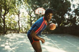 Earvin "Magic" Johnson, played by Quincy Isaiah, dribbles a basketball on a court in season 2 episode 1 of Winning Time: The Rise of the Lakers Dynasty