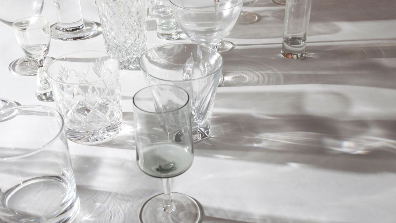 A white table with glasses on it, a light casting a shadow through them