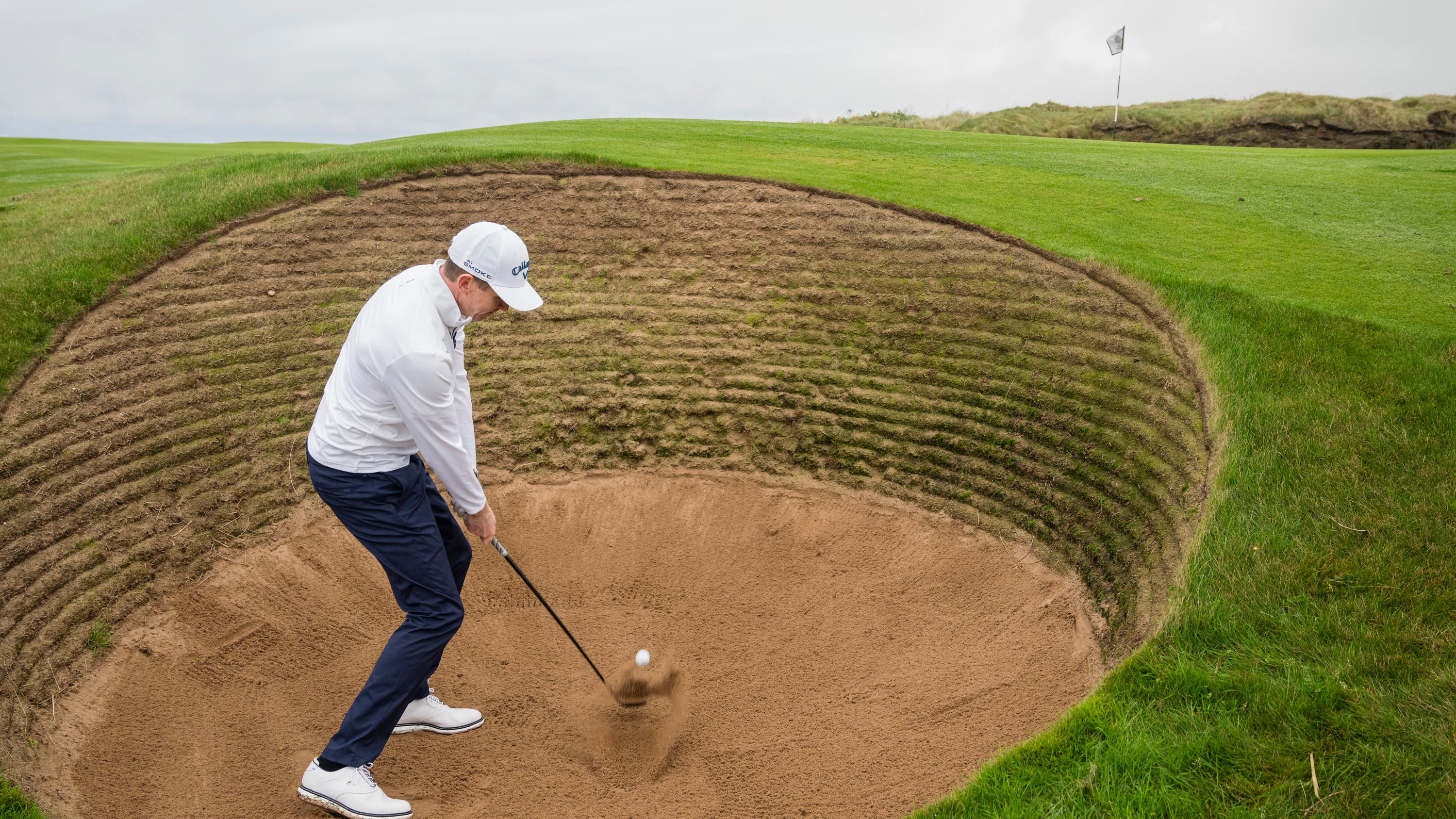 Ben Emerson at impact in the a greenside bunker with a revetted face, demonstrating the correct position during the low point of the swing