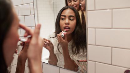 Woman applying lipstick while reflecting in mirror 