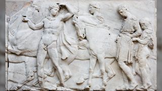 The Elgin Marbles stolen from Greece. From left to right we see a horse, a naked Greek man leading the way, whilst looking back at the others. Then there's another horse. Next to the horse is a person, and behind the horse if a person clothed in a tunic and a child with cloth draped around their shoulders.