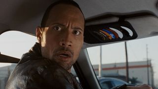 Dwayne Johnson wears a shocked face while looking into the driver's seat of his taxi cab